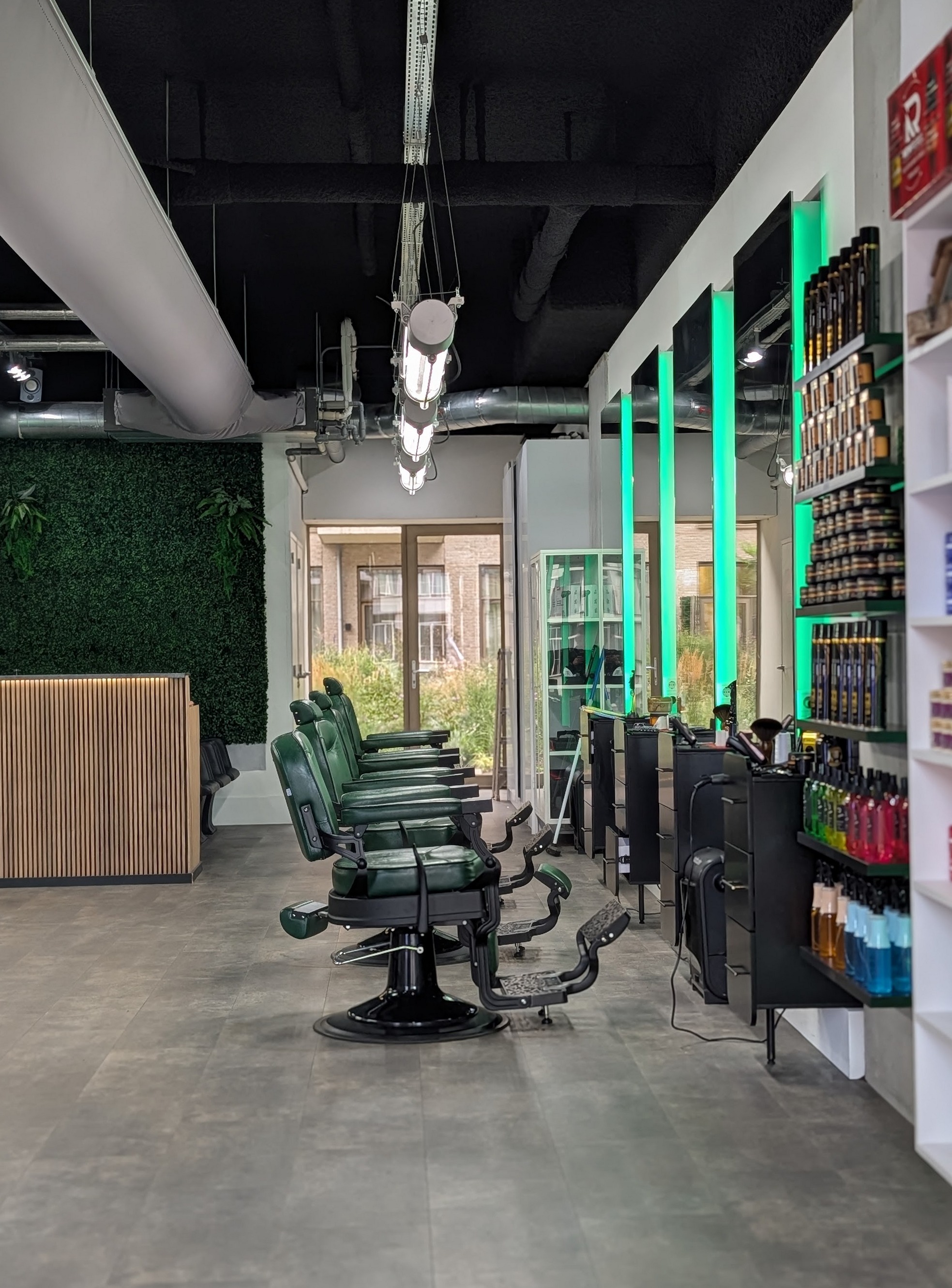 Zicht door de zaak langs de rij barberstoelen, met de productwand rechts en ledverlichting langs de spiegels